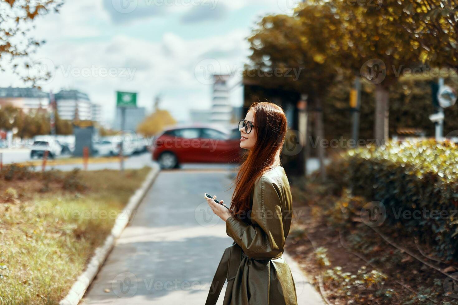 A woman in stylish trendy clothes walking down the street in the city and holding a navigator phone with a route photo