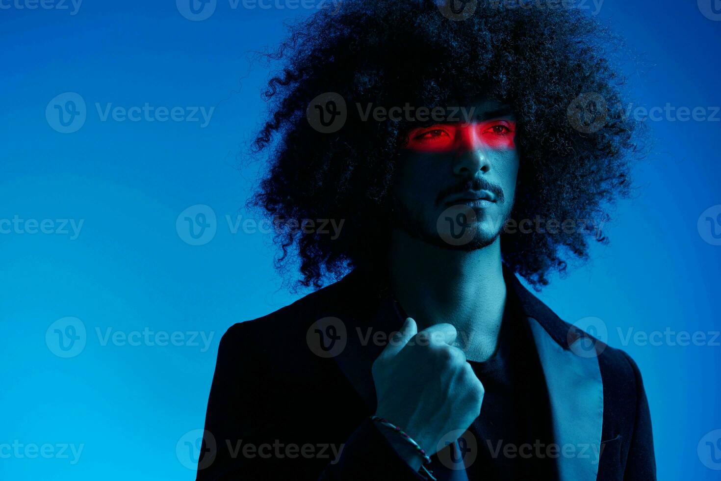 Fashion portrait of a man with curly hair on a blue background with a red stripe of light, multicolored light, trendy, modern concept. photo