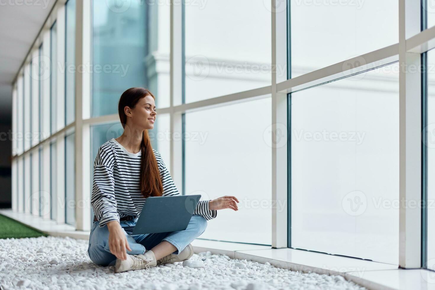 A woman freelancer sits with her laptop near a window overlooking the city and orders purchases online, the concept of online shopping, a copy space photo