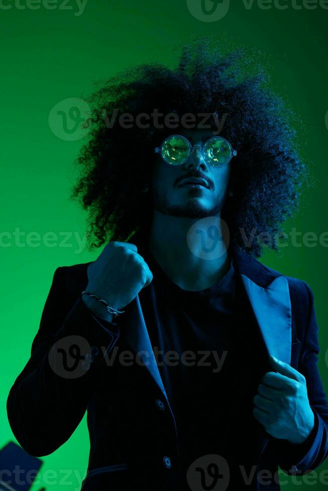 Fashion portrait of a man with curly hair on a green background with sunglasses, multinational, colored pink light, trendy, modern concept. photo