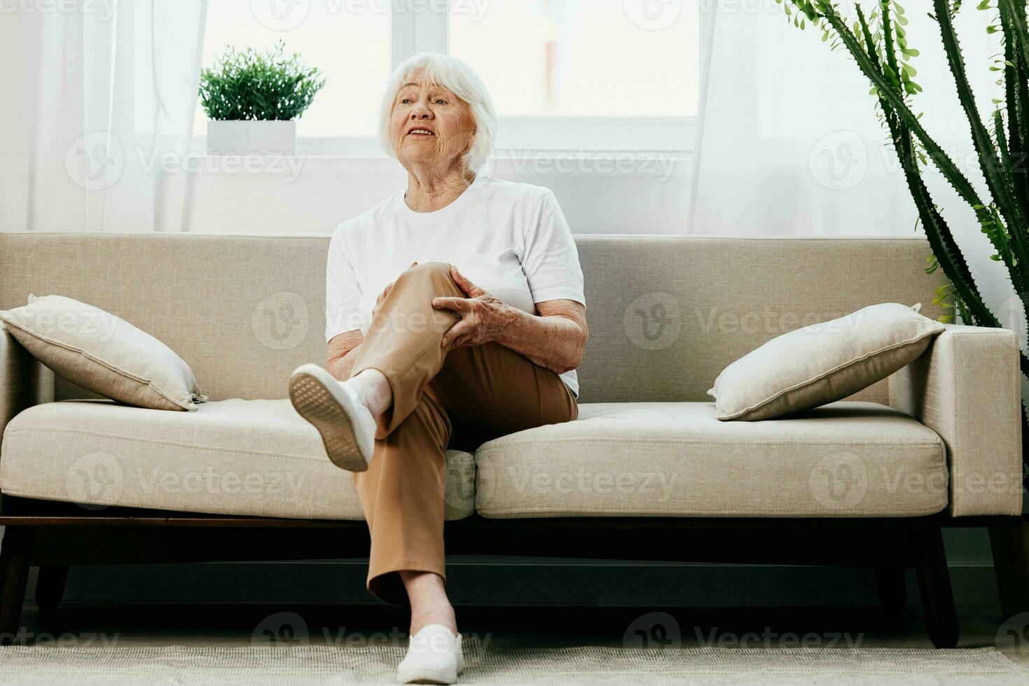 mayor mujer grave dolor en su pierna sentado en el sofá, salud problemas en antiguo edad, pobre calidad de vida. abuela con gris pelo sostiene en a su dolorido rodilla, problemas con articulaciones y ligamentos foto