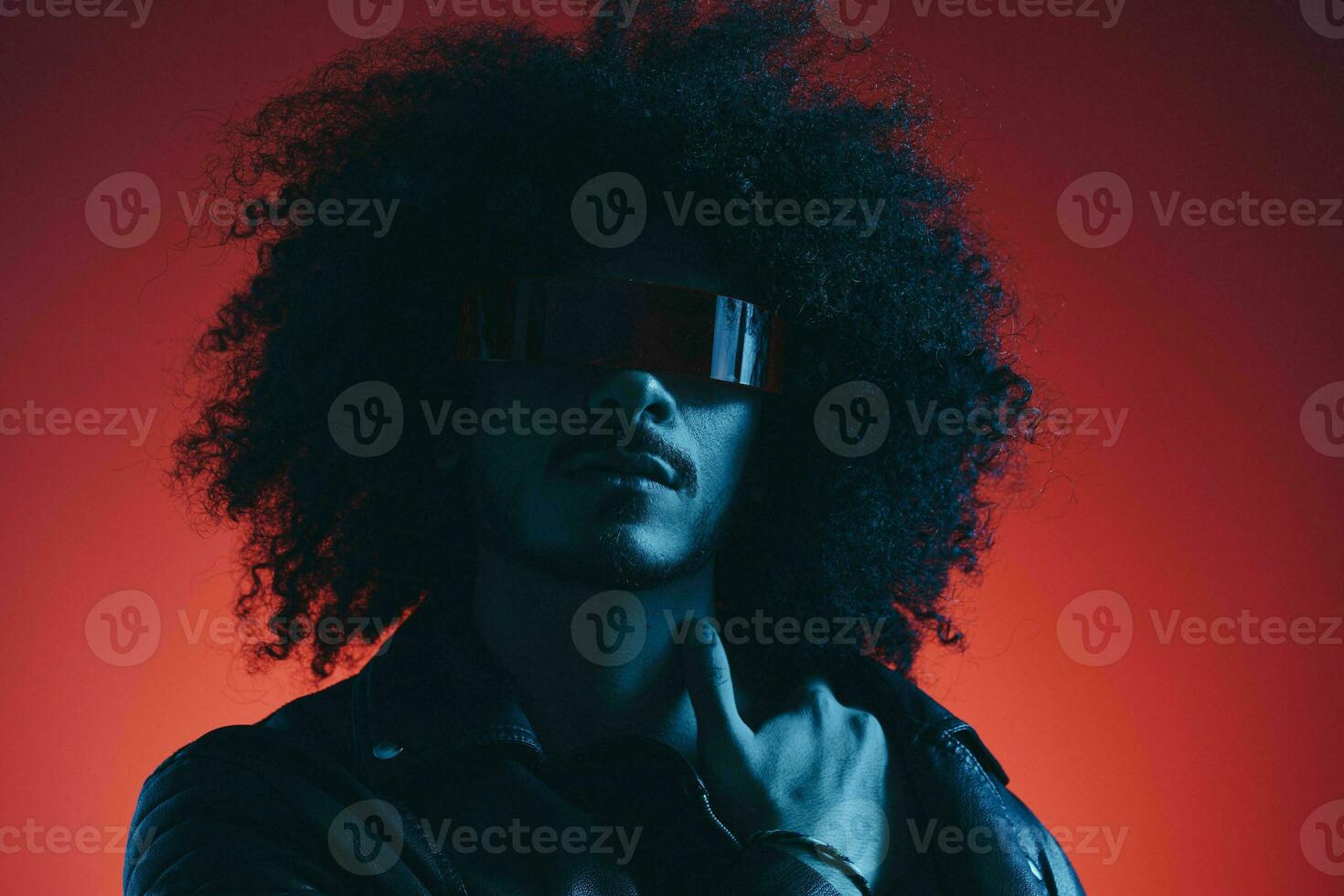 Portrait of fashion man with curly hair on red background with stylish glasses, multicultural, colored light, black leather jacket trend, modern concept. photo