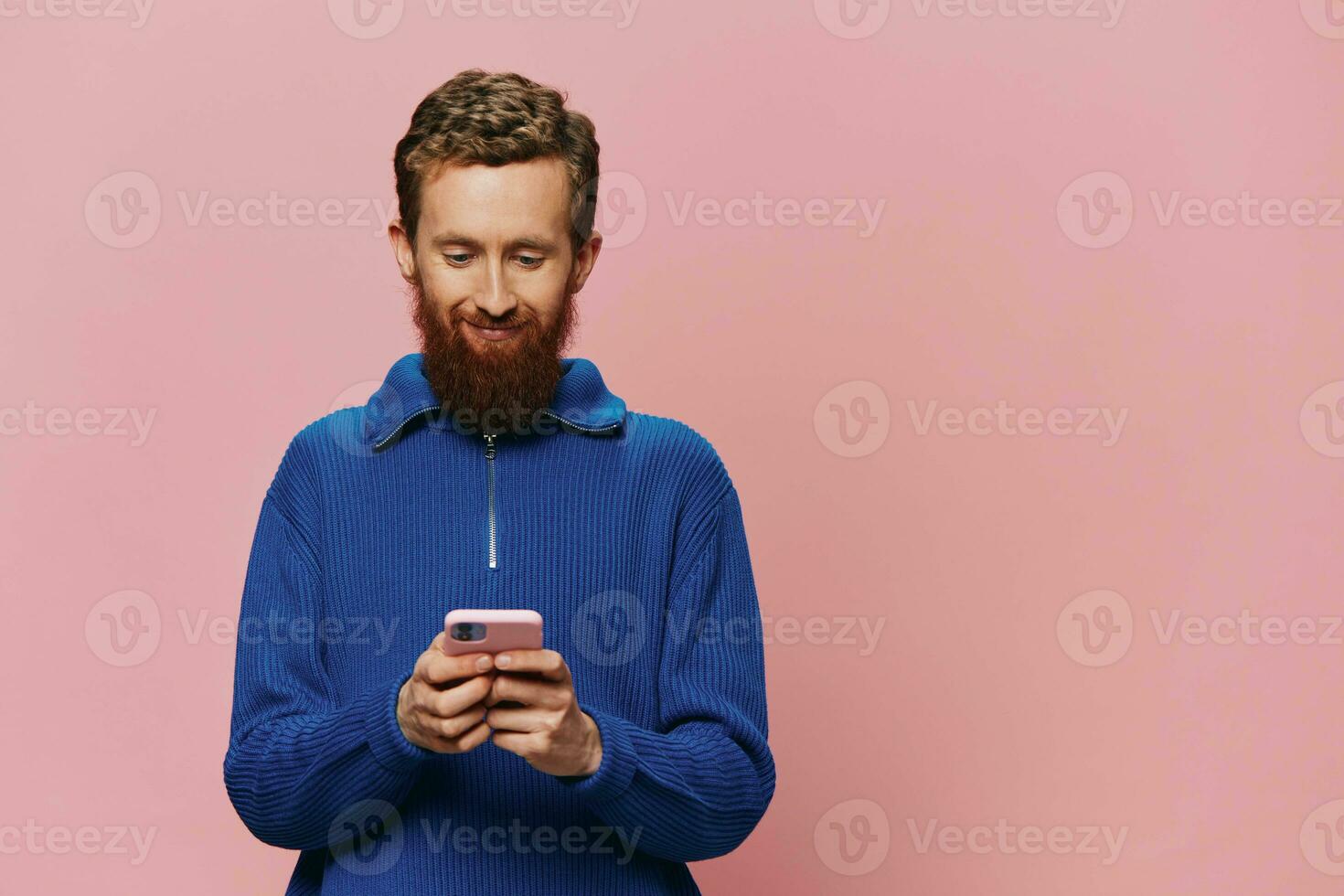Portrait of a man with a phone in his hands doing looking at it and talking on the phone, on a pink background. Communicating online social media, lifestyle photo