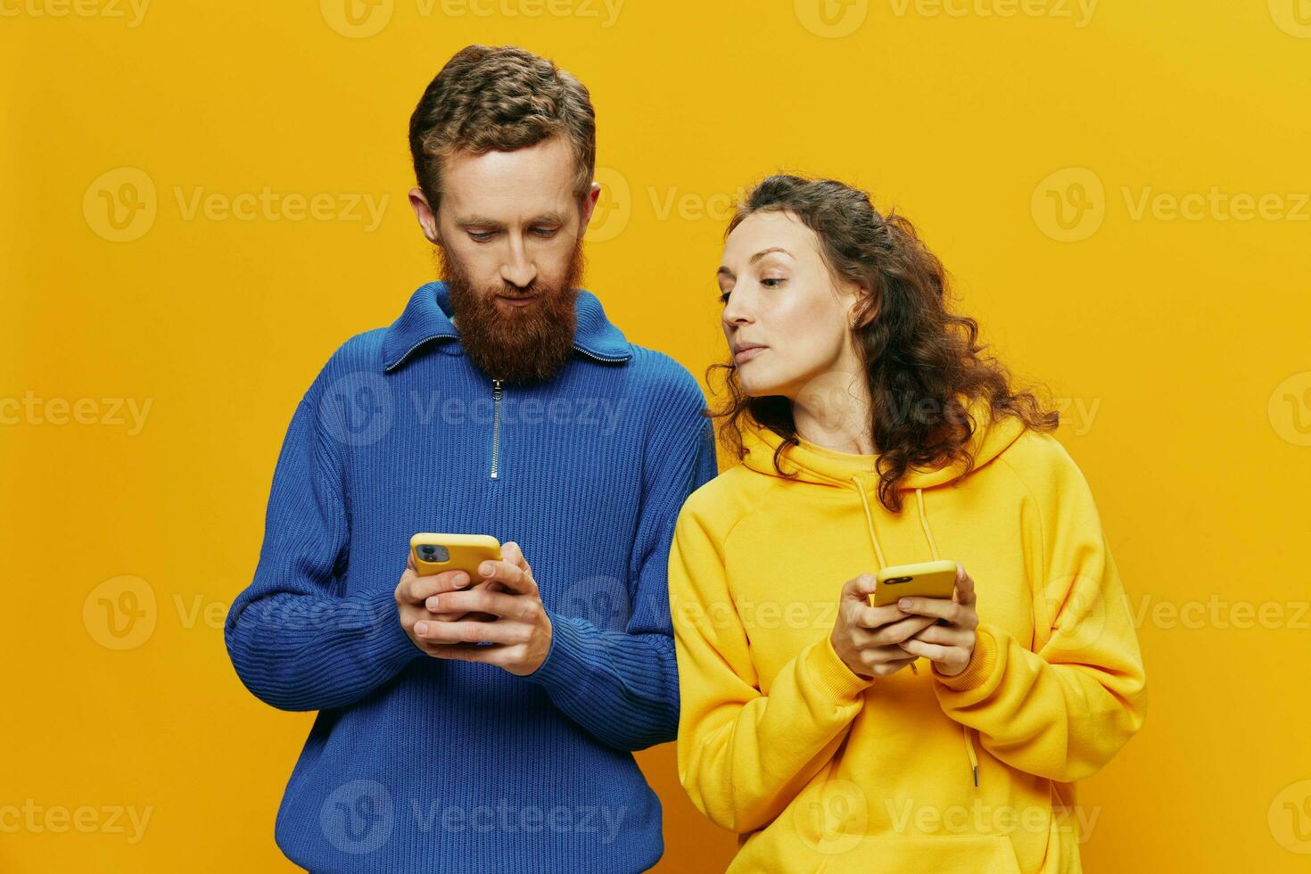 Woman man cheerful couple with phones in hand social networking and communication crooked smile fun and fight, in yellow background. The concept of real family relationships, freelancers, work online. photo