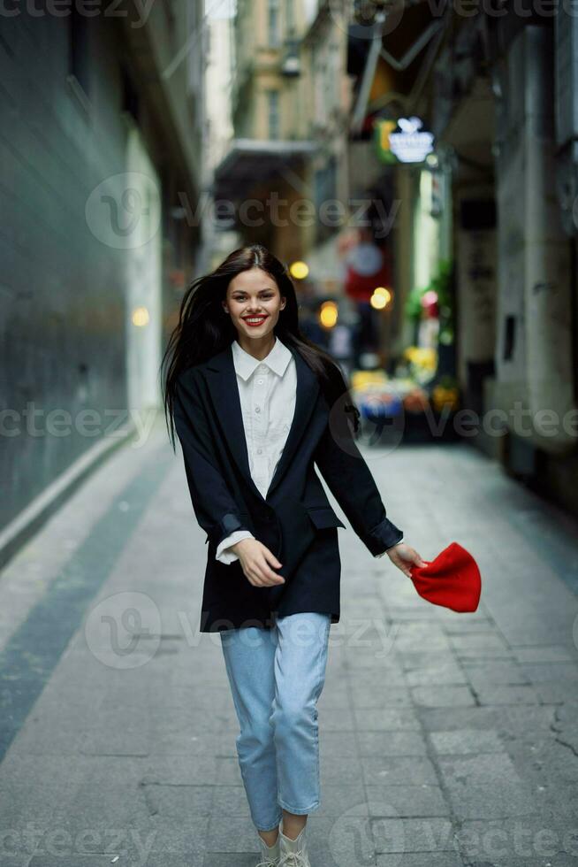 Moda mujer turista en elegante ropa en un chaqueta y rojo boina corriendo abajo el estrecho calle de el ciudad sonrisa y felicidad viaje, estilo, cinematográfico 25037499 Foto stock