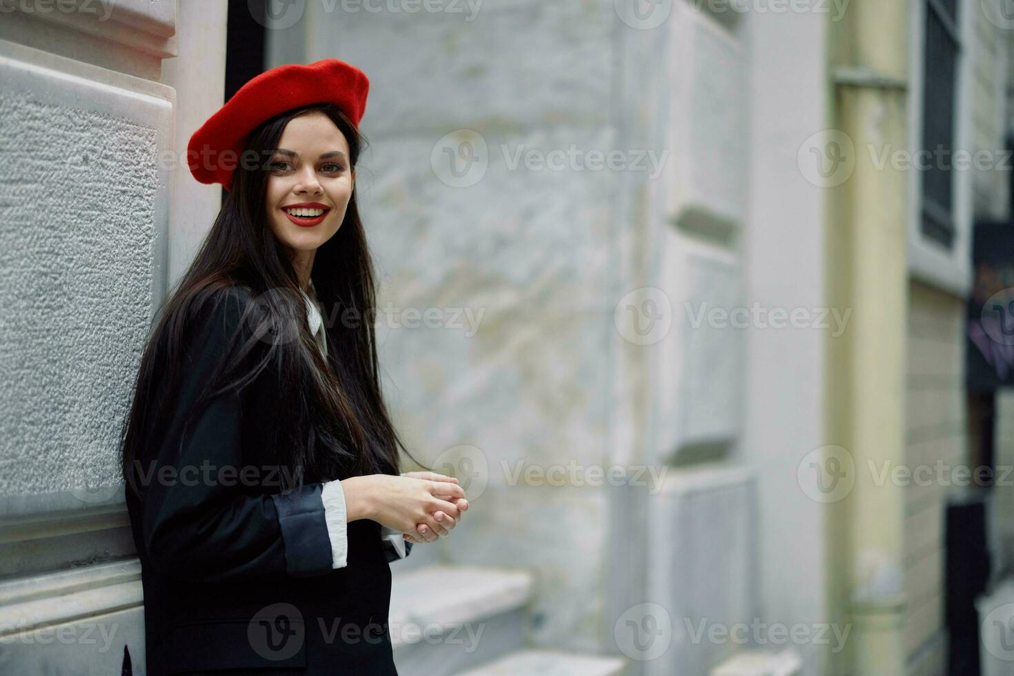 A woman standing near a wall in the city wearing a stylish jacket and a red beret with red lips, traveling. photo