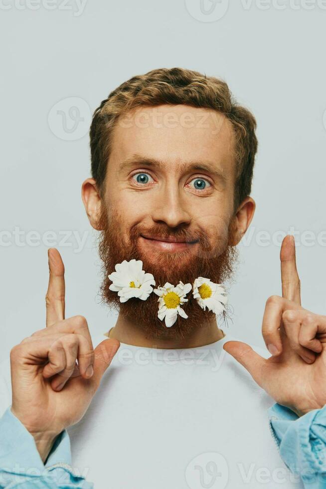 Portrait of a funny man in a white T-shirt with flowers daisies in his beard on a white isolated background, copy place. Holiday concept and congratulations. photo