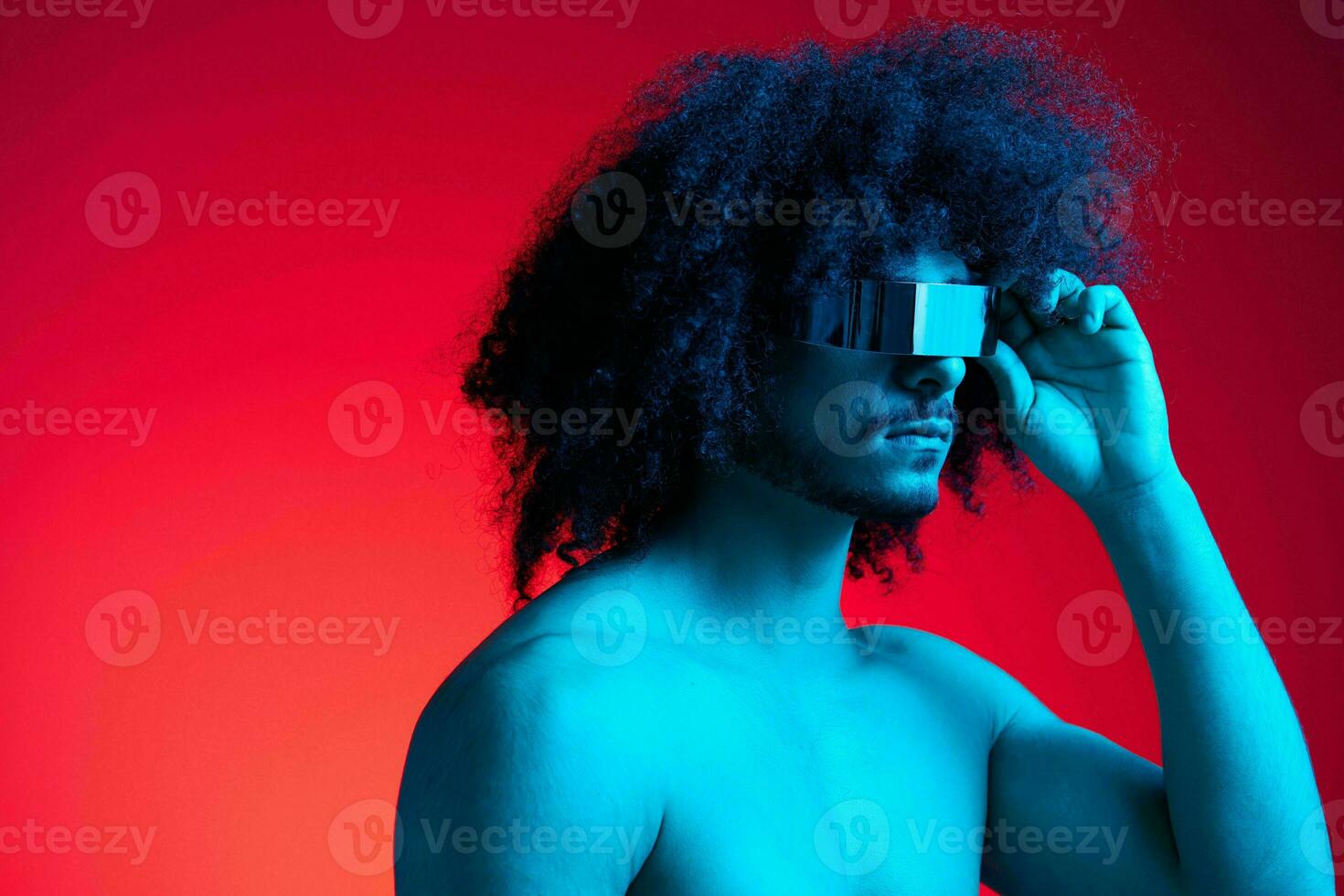 Portrait of fashion man with curly hair on red background with stylish glasses, multinational, colored light, black leather jacket trend, modern concept, sexy body. photo