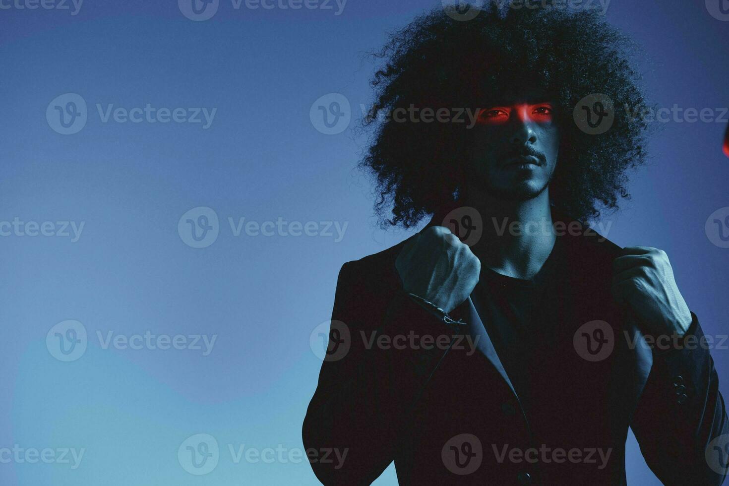 Fashion portrait of a man with curly hair on a blue background with a red stripe of light, multicolored light, trendy, modern concept. photo