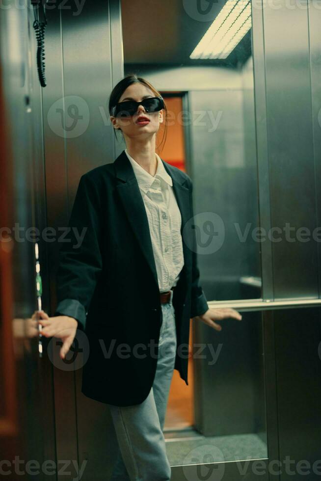 elegante mujer en negro chaqueta y Gafas de sol posando en ascensor, Moda modelo, oscuro cinematográfico ligero y color foto