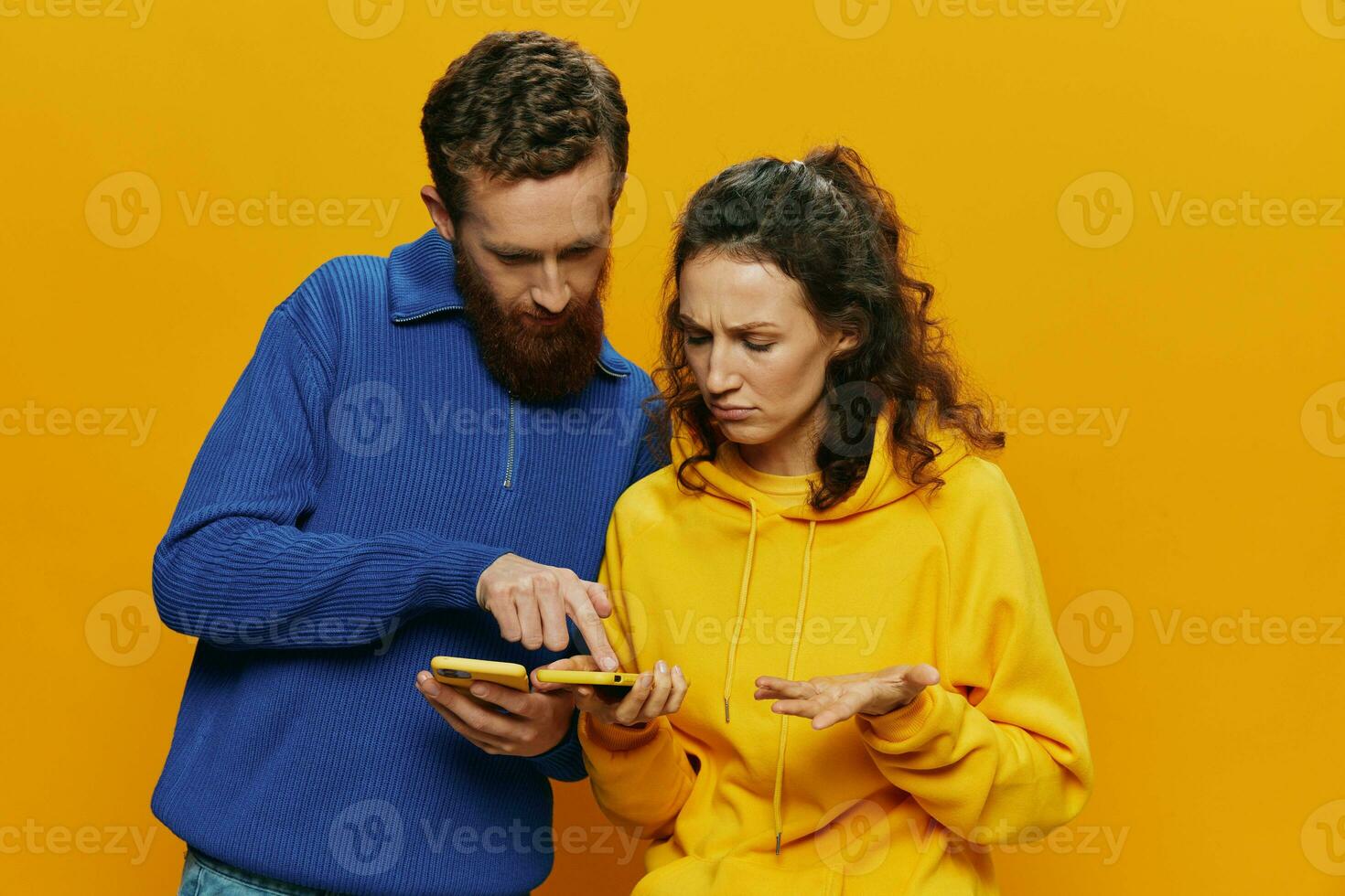 Woman man cheerful couple with phones in hand social networking and communication crooked smile fun and fight, in yellow background. The concept of real family relationships, freelancers, work online. photo