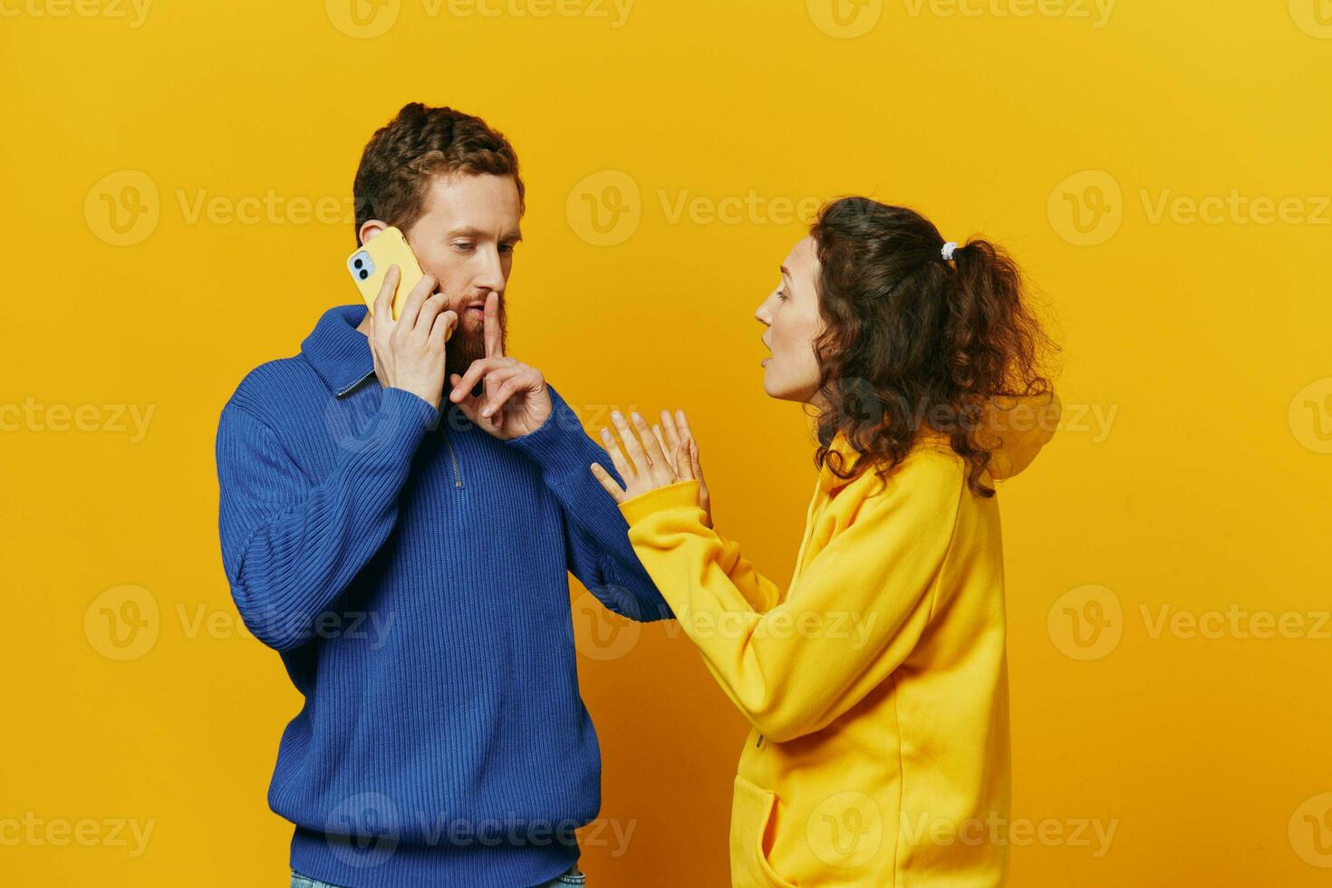 Man and woman couple with phone in hand call talking on the phone, on a yellow background, symbols signs and hand gestures, family quarrel jealousy and scandal. photo