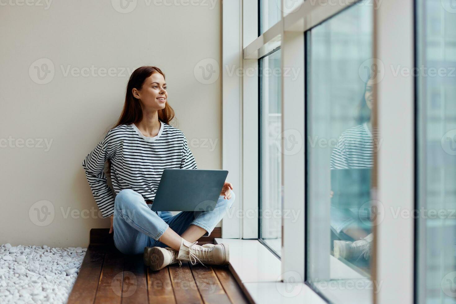 Business woman sitting with a laptop at the window full-length and smiling with teeth and looking out the window, happy woman work online in the office, copy place photo