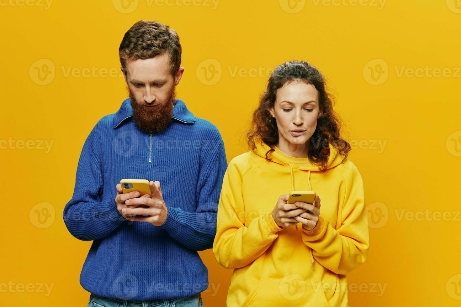Woman man cheerful couple with phones in hand social networking and communication crooked smile fun and fight, in yellow background. The concept of real family relationships, freelancers, work online. photo