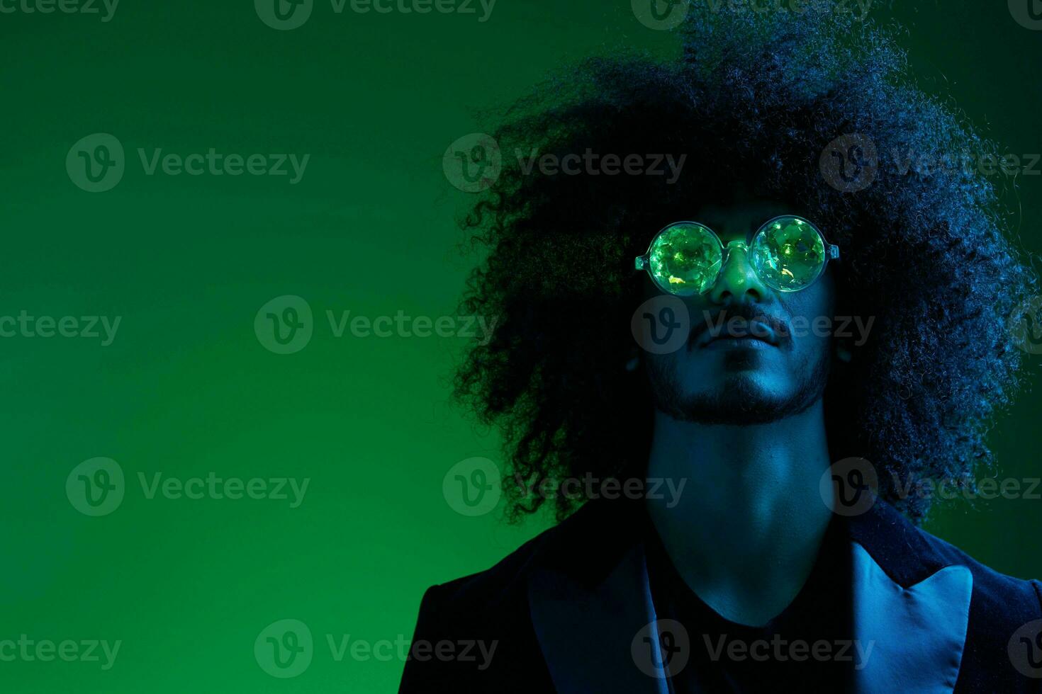 Fashion portrait of a man with curly hair on a green background with sunglasses, multinational, colored pink light, trendy, modern concept. photo