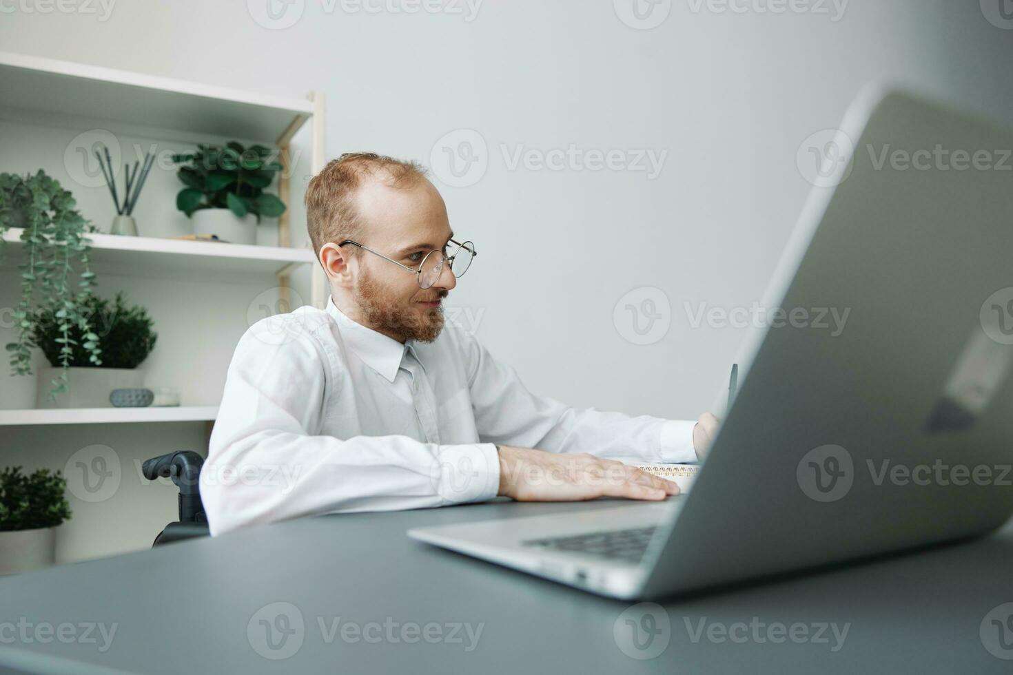 A man wheelchair businessman in the office works at a laptop, writing down ideas and a plan in a notebook, thoughtfulness, integration into society, the concept of working a person with disabilities photo