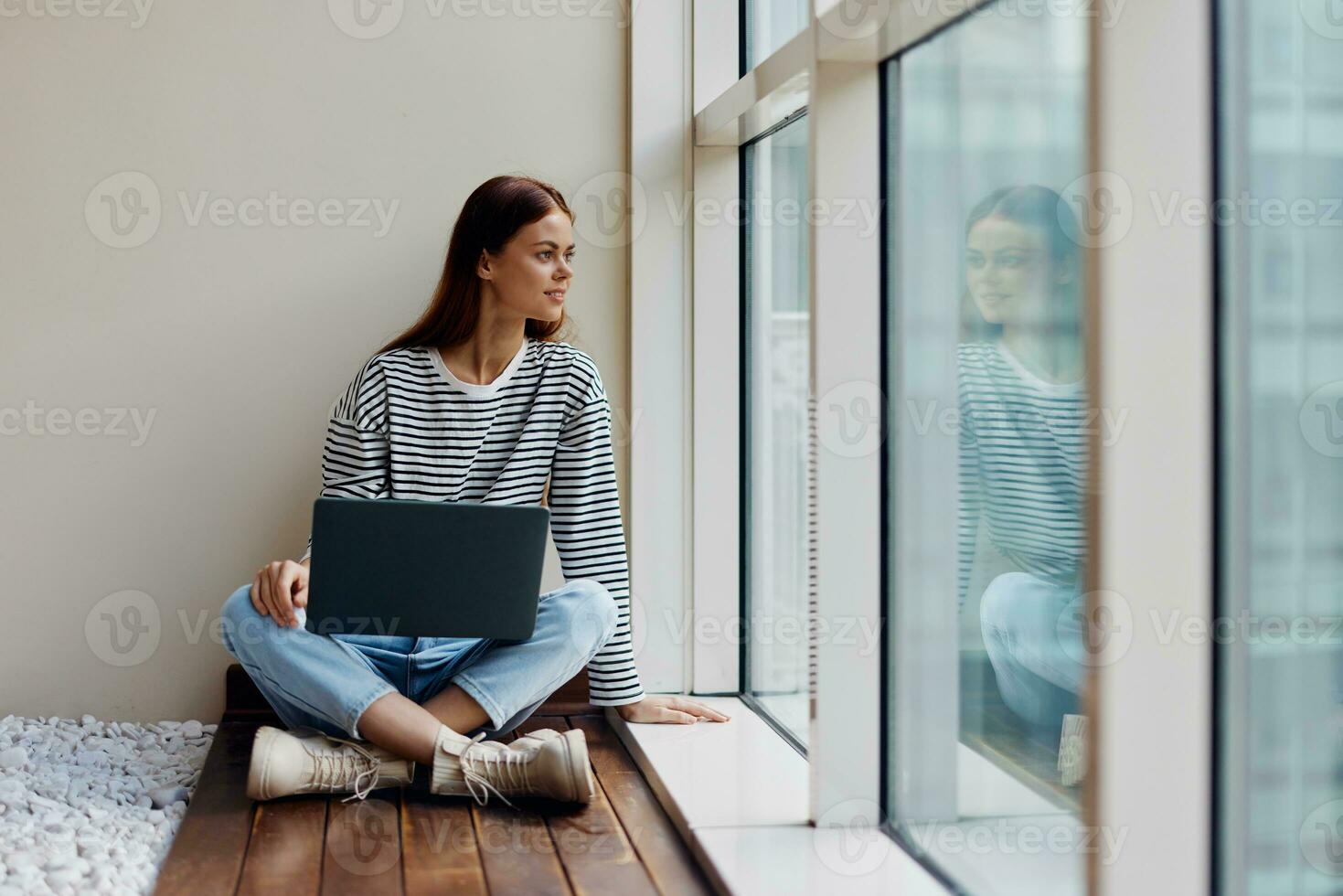 Business woman sitting with a laptop at the window full-length and smiling, happy woman work online in the office, copy space photo