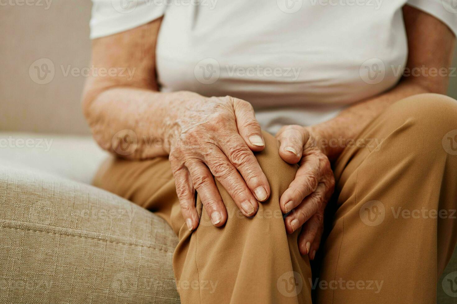 Elderly woman severe pain in her leg sitting on the couch, health problems in old age, poor quality of life. Grandmother with gray hair holds on to her sore knee, problems with joints and ligaments. photo