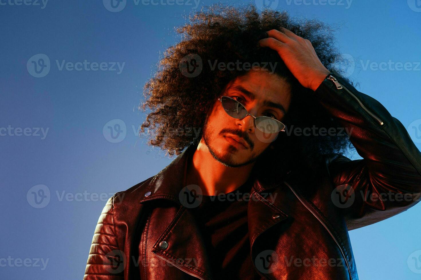 Portrait of a stylish man with curly hair on a blue background multinational, colored light, trendy glasses, modern concept. photo