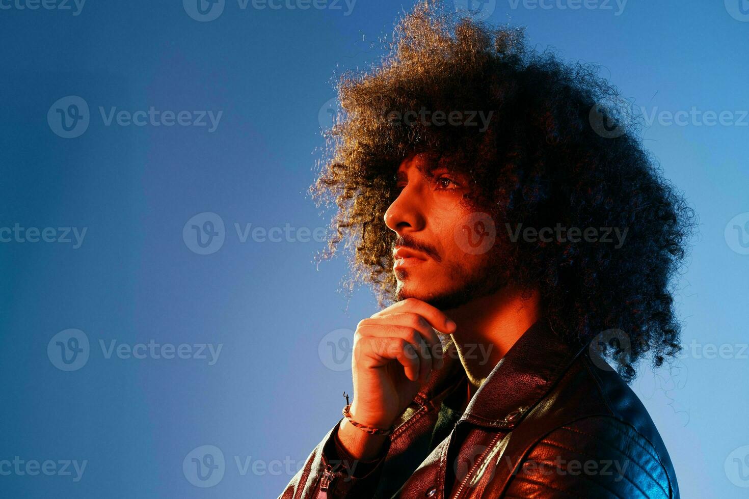 Portrait of a stylish man with curly hair in smoke on a blue background multinational, color light, trendy, modern concept. photo