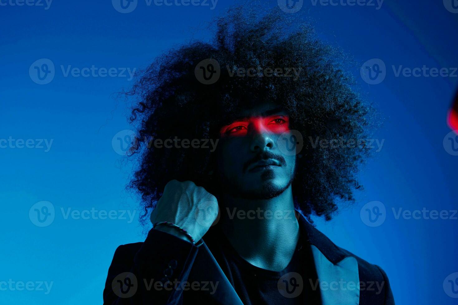 Fashion portrait of a man with curly hair on a blue background with a red stripe of light, multicolored light, trendy, modern concept. photo
