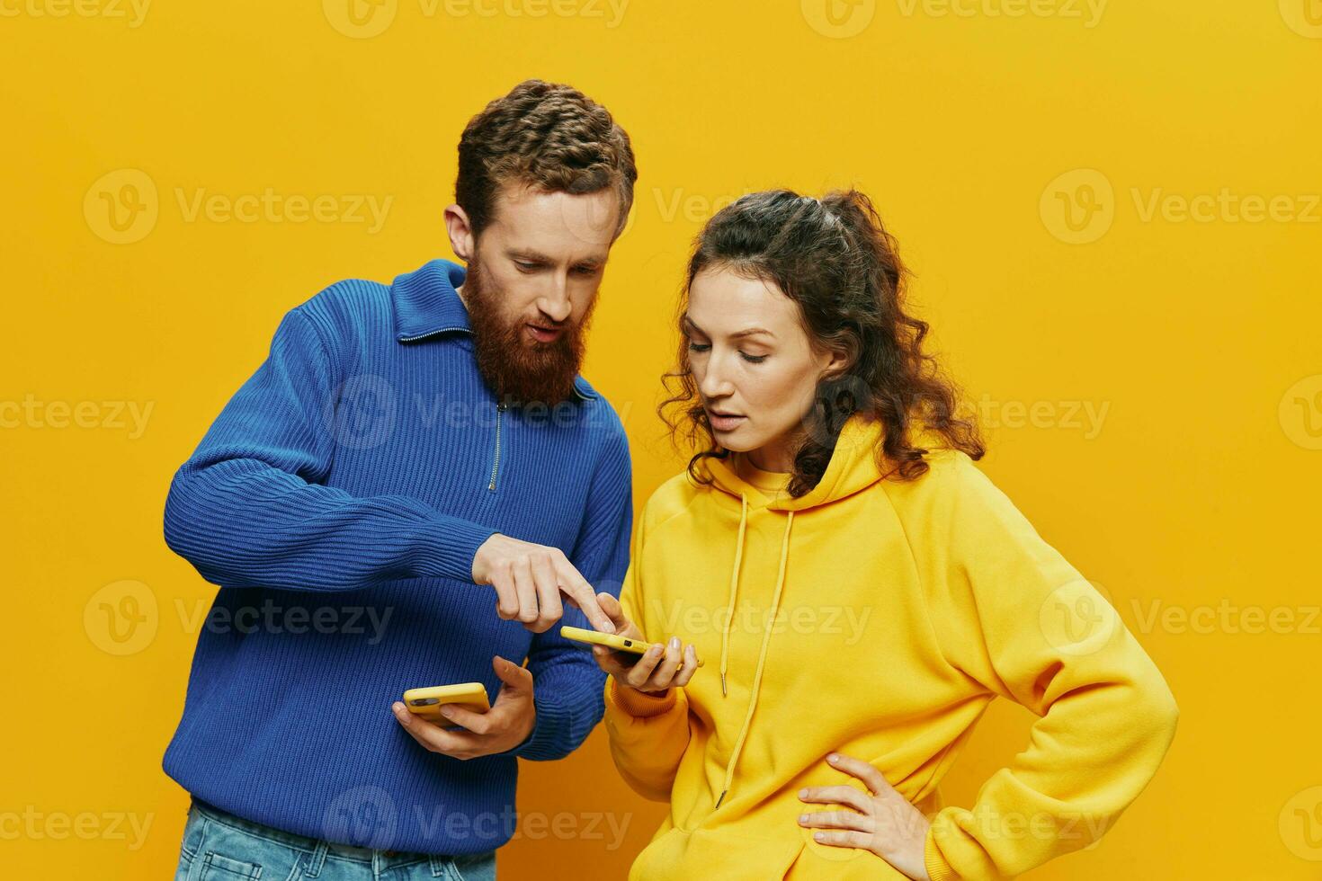 Woman man cheerful couple with phones in hand social networking and communication crooked smile fun and fight, in yellow background. The concept of real family relationships, freelancers, work online. photo