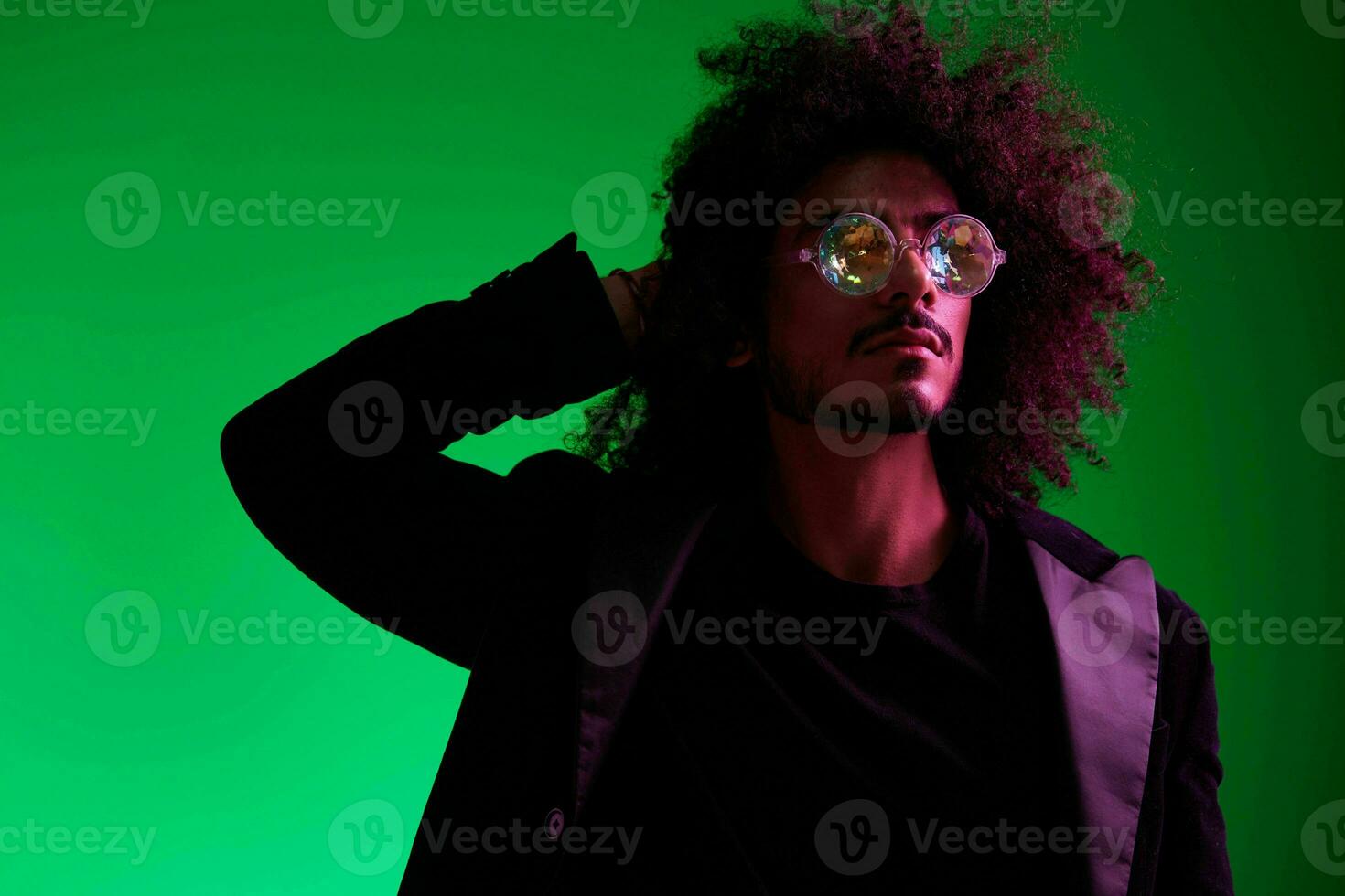 Fashion portrait of a man with curly hair on a green background with sunglasses, multinational, colored pink light, trendy, modern concept. photo