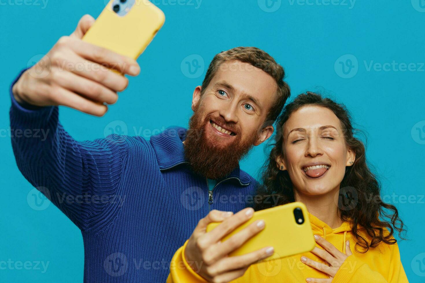 Woman and man funny couple with phones in hand taking selfies crooked smile fun, on blue background. The concept of real family relationships, talking on the phone, work online. photo