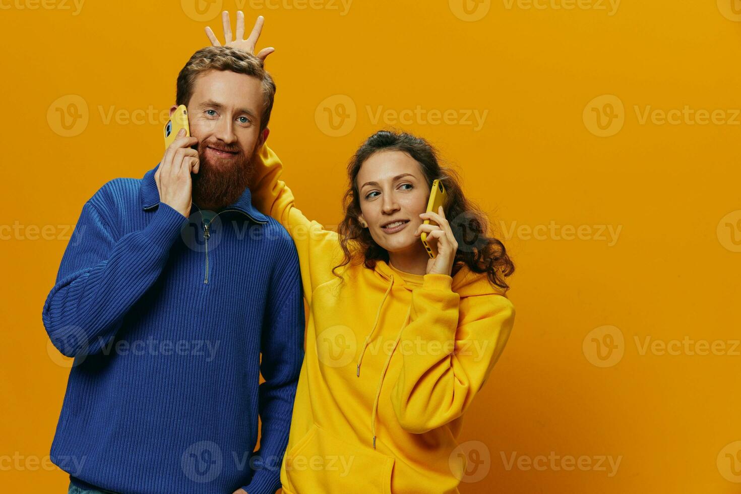 Woman and man cheerful couple with phones in hand talking on cell phone crooked smile cheerful, on yellow background. The concept of real family relationships, talking on the phone, work online. photo
