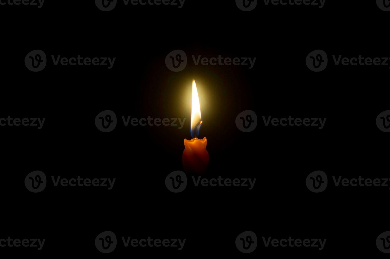 A single burning candle flame or light glowing spiral orange candle on black or dark background on table in church for Christmas, funeral or memorial service with copy space photo