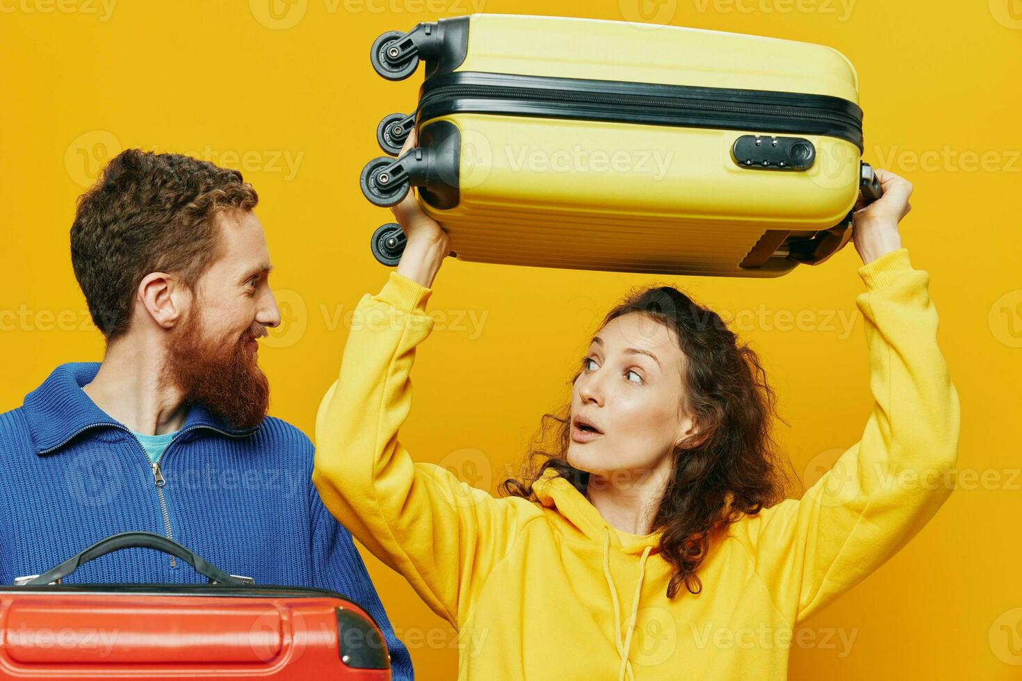 Woman and man smiling, suitcases in hand with yellow and red suitcase smiling merrily and crooked, yellow background, going on a trip, family vacation trip, newlyweds. photo