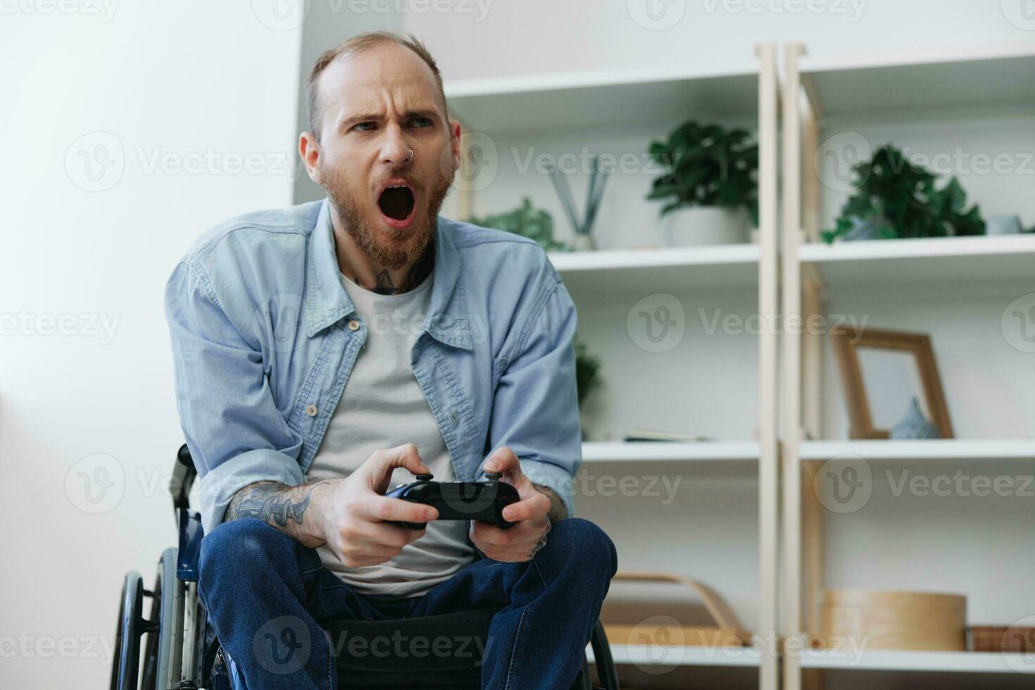 A man in a wheelchair gamer plays games with a joystick in his hands at home, anger and sadness from losing, copy space, with tattoos on his hands, health concept man with disabilities, real person photo