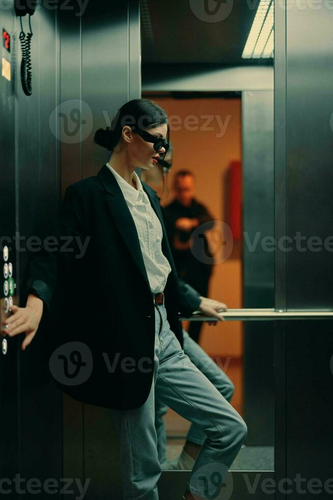 Stylish woman in black jacket and sunglasses posing in elevator, fashion model, dark cinematic light and color, glamor vintage photo