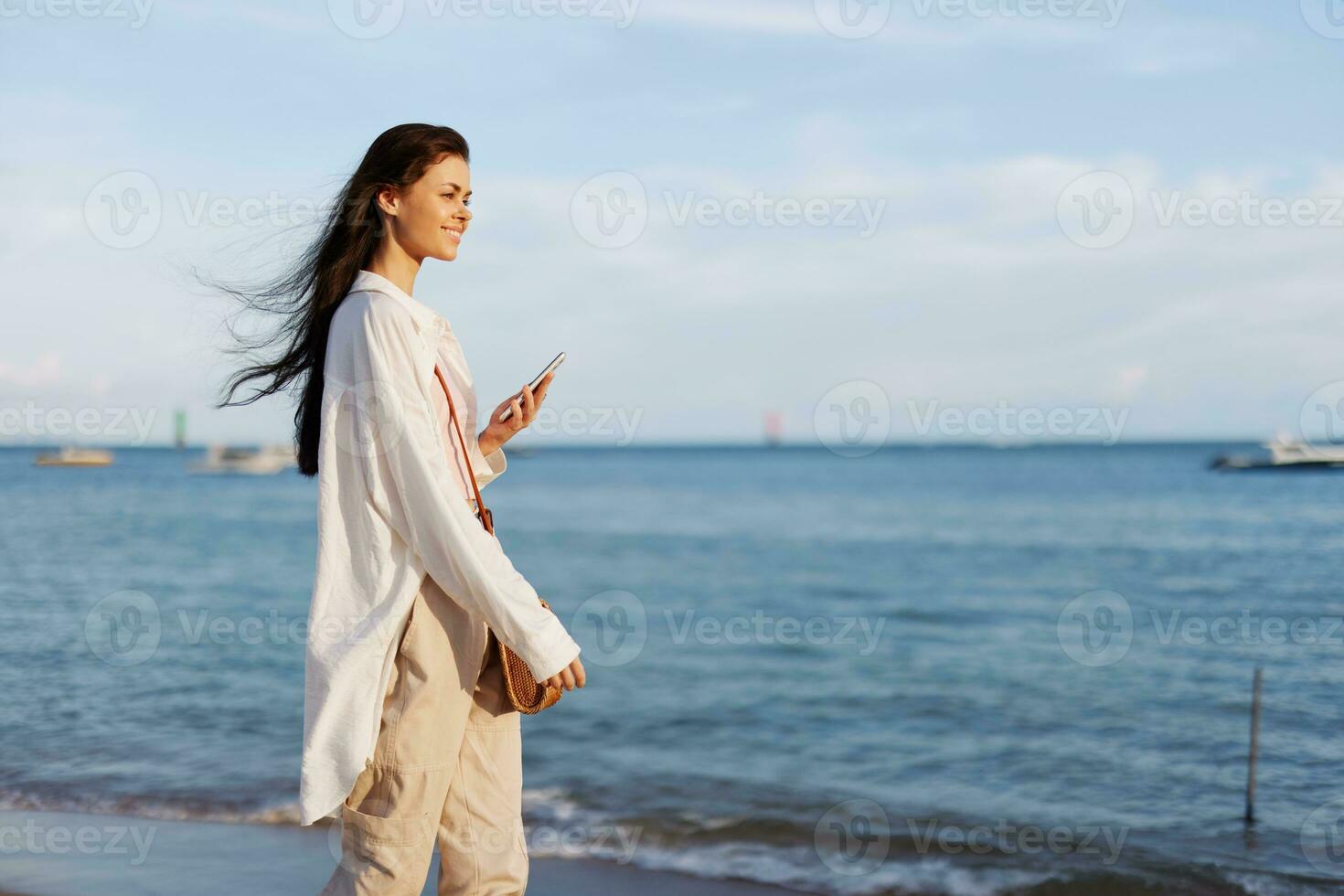 Freelance woman with phone in hand on vacation walking on the beach by the ocean in Bali, happy travel and vacation, mobile communications, Internet online photo