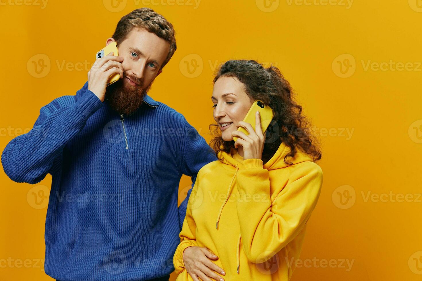 Man and woman couple smiling merrily with phone in hand social media viewing photos and videos, on yellow background, symbols signs and hand gestures, family freelancers.