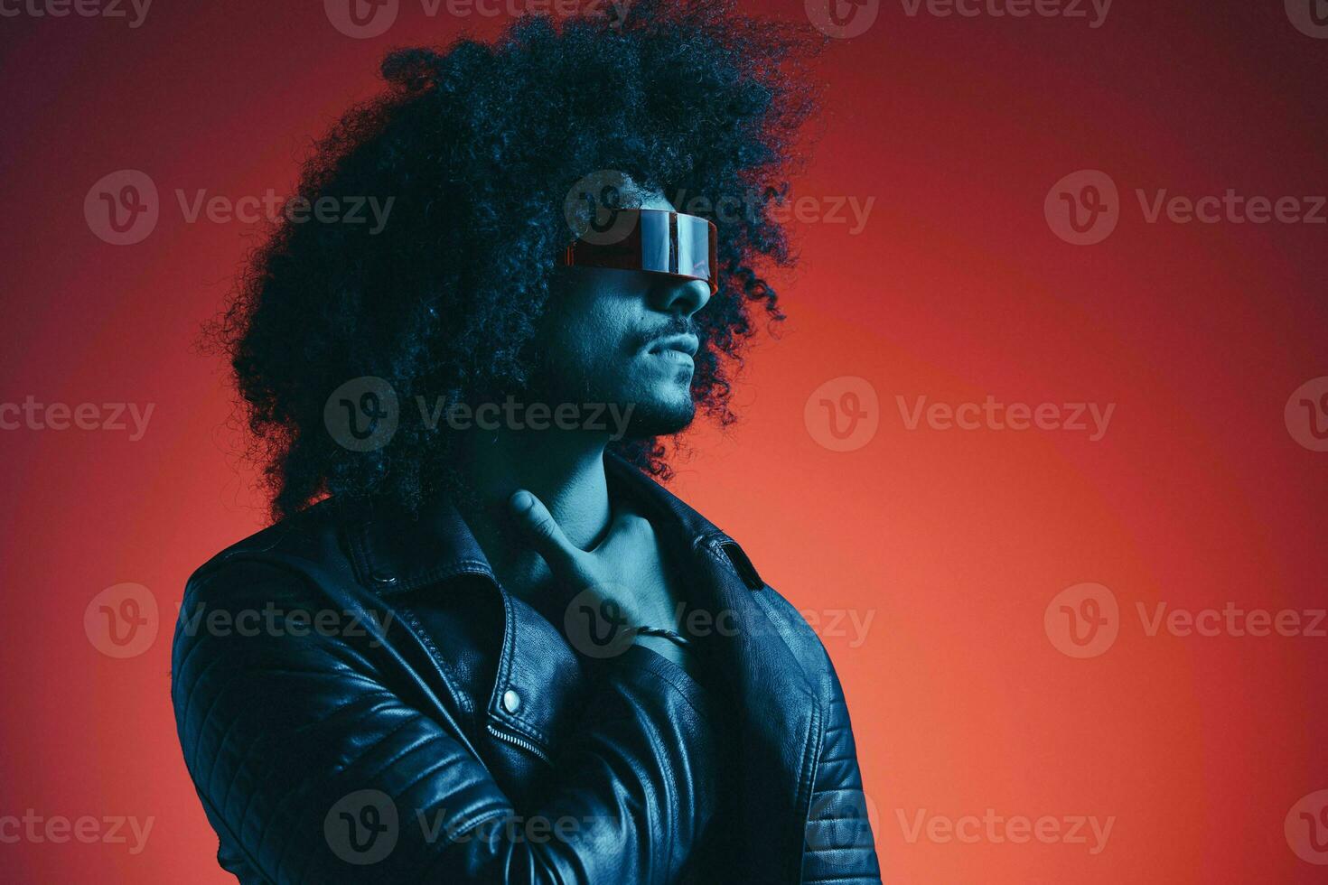 Portrait of fashion man with curly hair on red background with stylish glasses, multicultural, colored light, black leather jacket trend, modern concept. photo