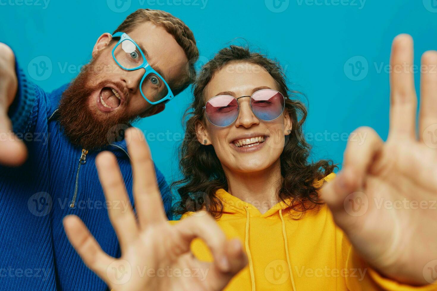 un mujer y un hombre divertido Pareja arrancando y demostración señales con su manos sonriente alegremente, en un azul fondo, el concepto de un real relación en un familia. foto