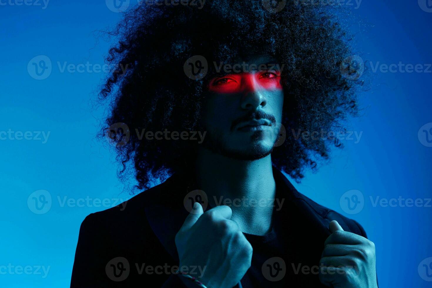 Fashion portrait of a man with curly hair on a blue background with a red stripe of light, multicolored light, trendy, modern concept. photo