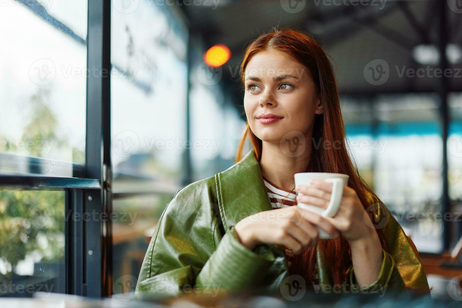 Portrait of a woman influencer drinking a drink from a mug in a cafe and smiling with her teeth looking out the window, content blogger close-up photo