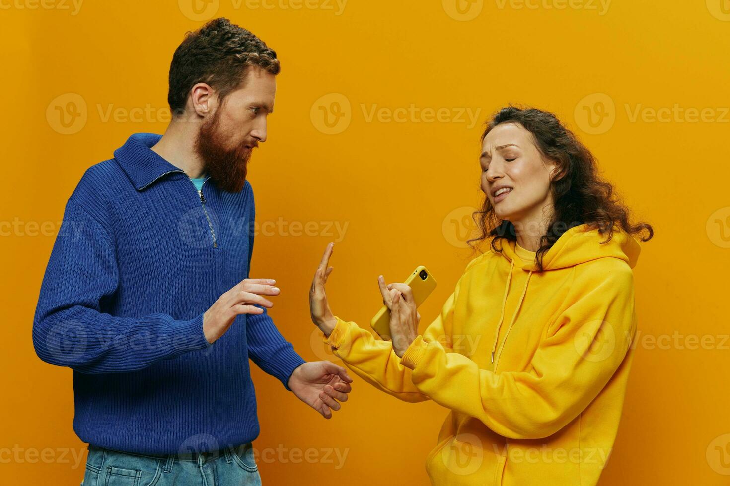 Woman man cheerful couple with phones in hand social networking and communication crooked smile fun and fight, in yellow background. The concept of real family relationships, freelancers, work online. photo