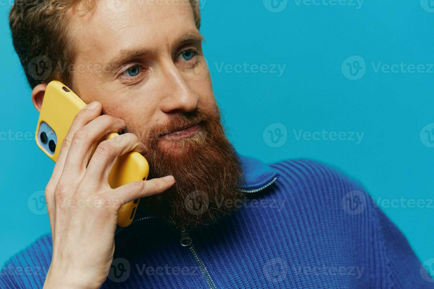 Portrait of a man with a phone in his hands does looking at it and talking on the phone, on a blue background. Communicating online social media, lifestyle photo