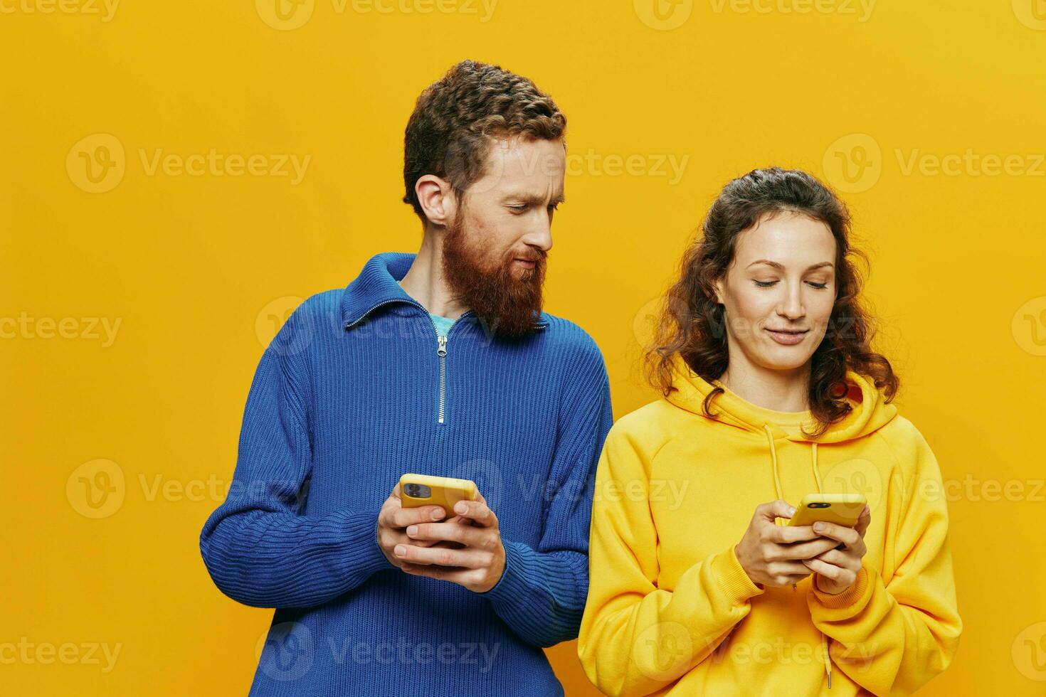Woman man cheerful couple with phones in hand social networking and communication crooked smile fun and fight, in yellow background. The concept of real family relationships, freelancers, work online. photo