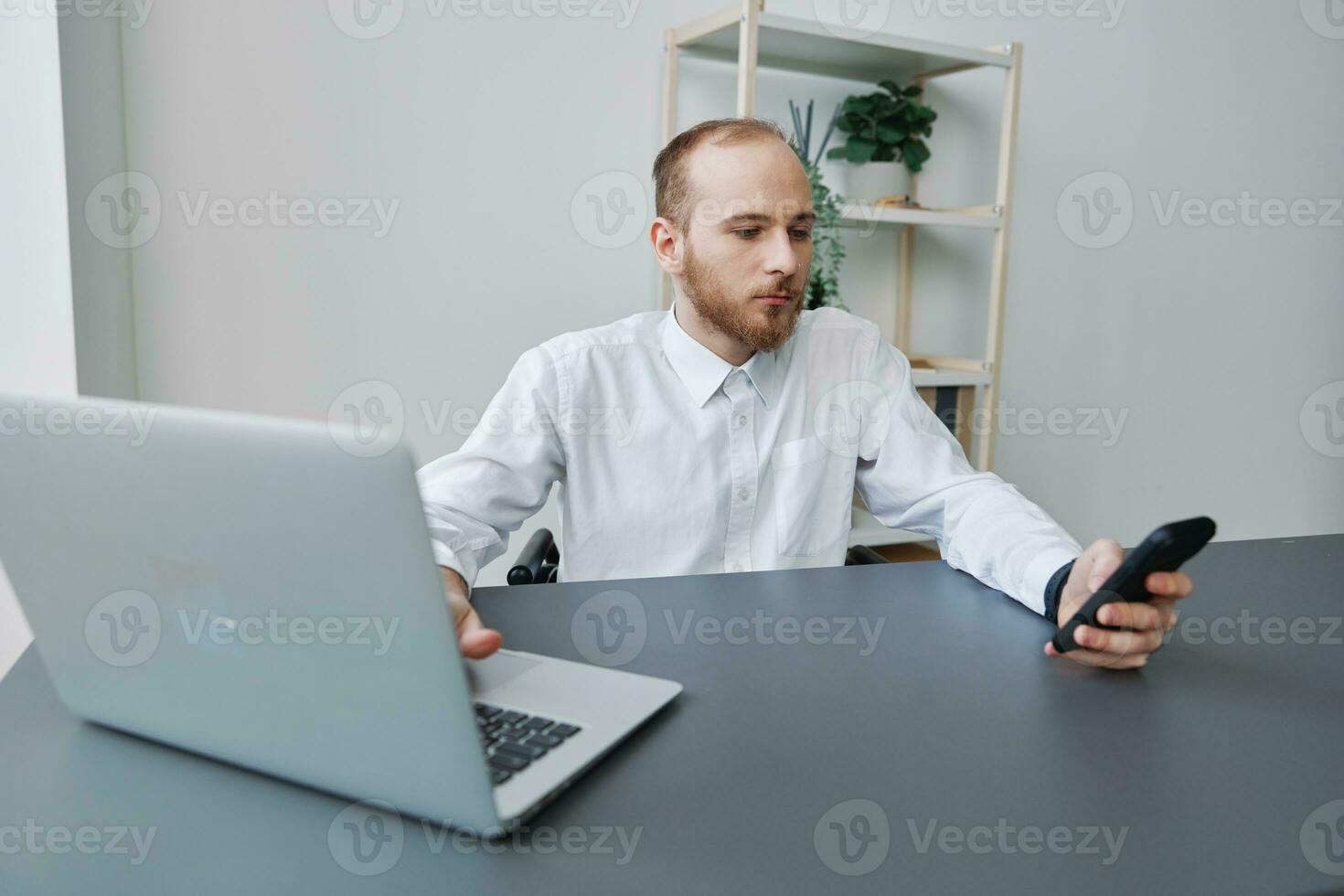 A man in a wheelchair a businessman in the office works at a laptop and holds a phone in his hands, thoughtfulness, integration into society, the concept of working a person with disabilities photo