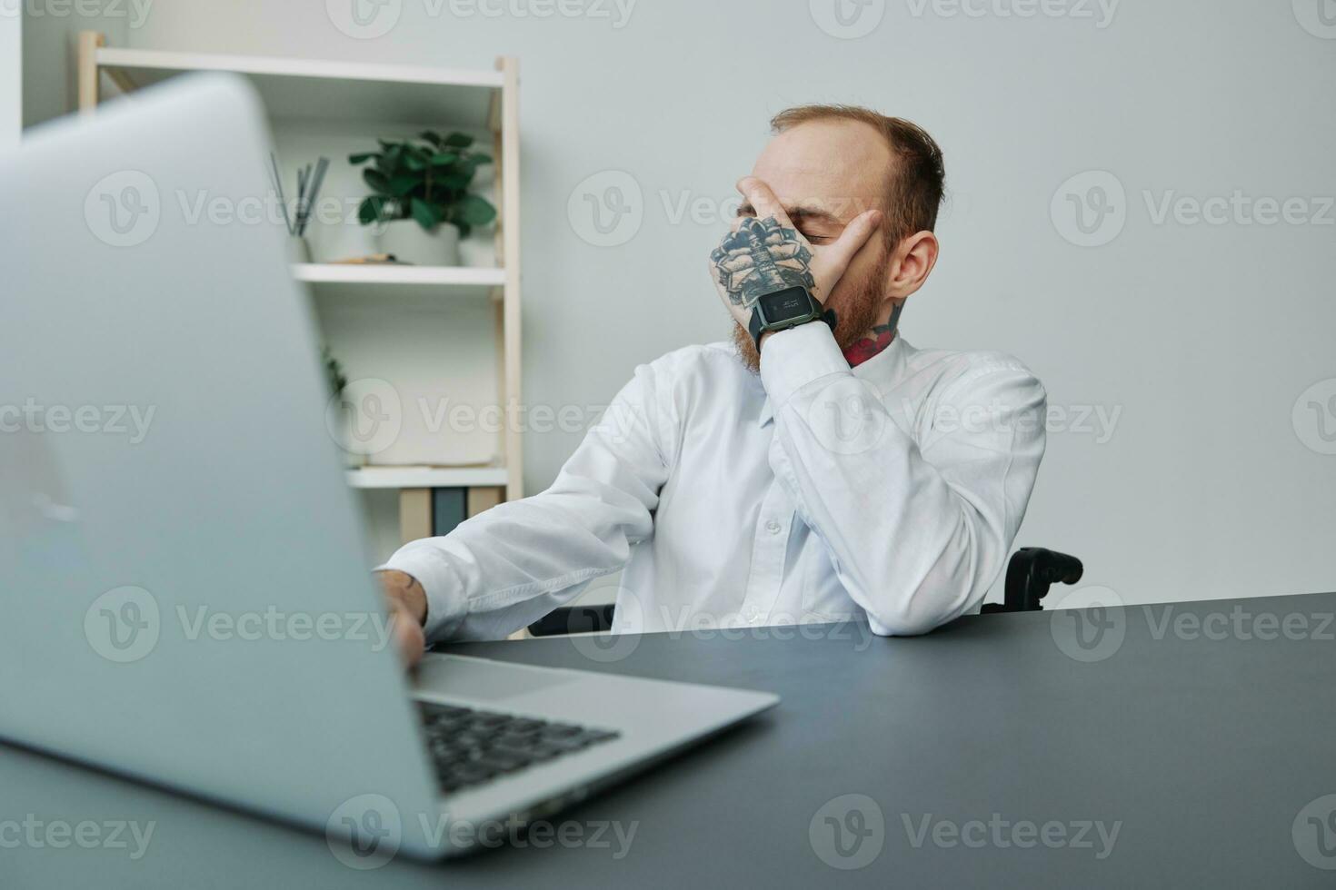 A man wheelchair, a businessman in an office at a laptop, fatigue and emotional burnout at the end of the working day, the concept of working a person with disabilities, freedom from social frameworks photo