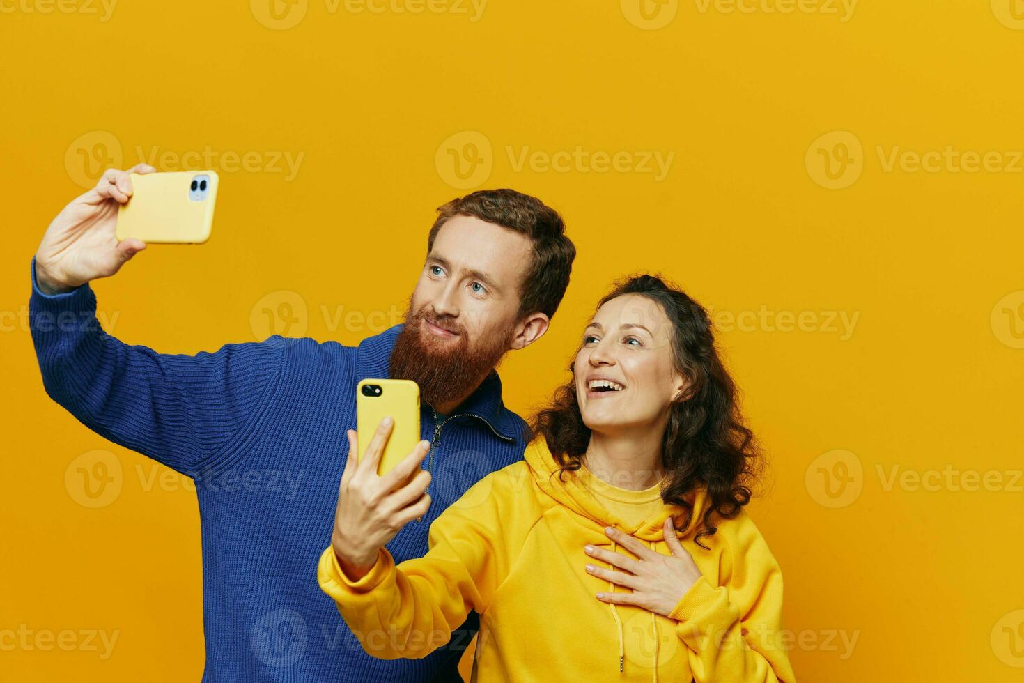 Man and woman couple smiling merrily with phone in hand social media viewing photos and videos, on yellow background, symbols signs and hand gestures, family freelancers.