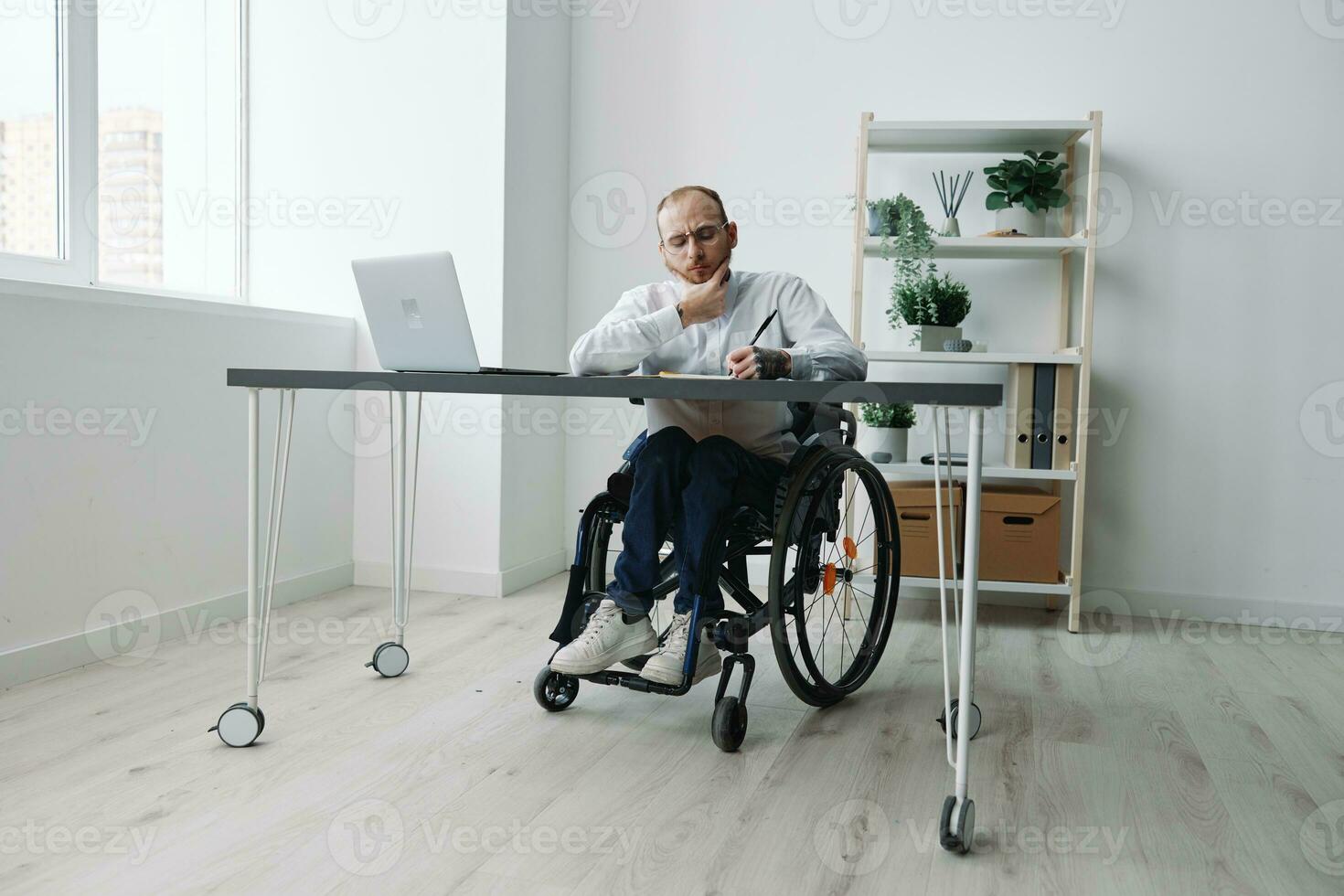 A man in a wheelchair, a businessman in the office works at a laptop, writing down a plan in a notebook, thoughtfulness, integration into society, the concept of working a person with disabilities photo