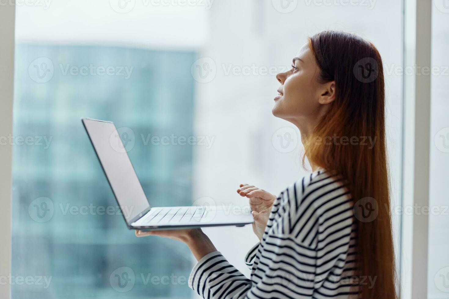 Woman student studying in the city near a window and holding a laptop, working with technology online, smiling photo