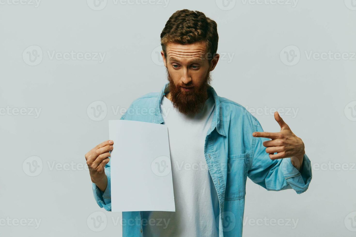 retrato de un adulto masculino en un gris antecedentes con un blanco sábana de papel en su manos para tu diseño y texto, disposición, Copiar espacio, espacio para texto, dedo señalando foto