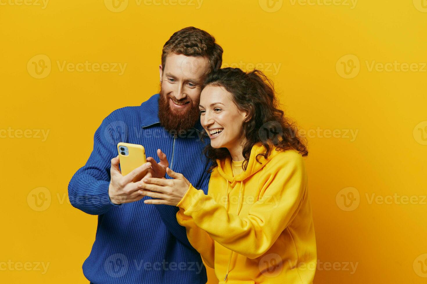 Man and woman couple smiling merrily with phone in hand social media viewing photos and videos, on yellow background, symbols signs and hand gestures, family freelancers.