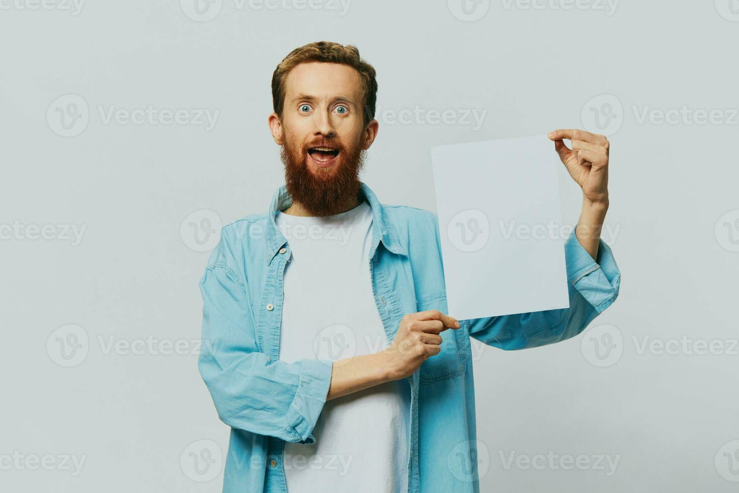 Portrait of an adult male on a gray background with a white sheet of paper in his hands for your design and text, layout, copy space, space for text, finger pointing photo